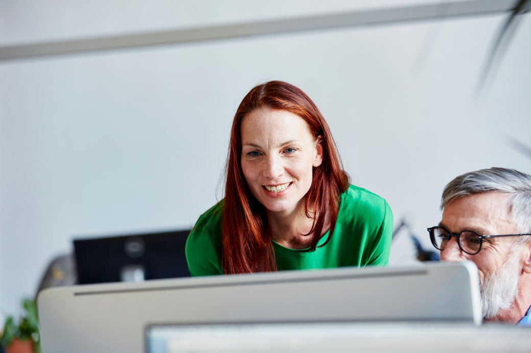 smiling woman looking at a computer screen over the shoulder of an older man