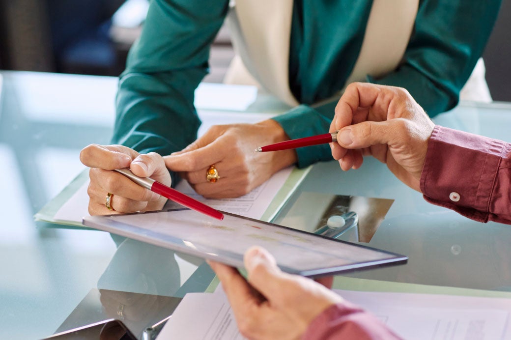 close-up photo of a woman's and man's hands each holding pens and collaborating on high reliability healthcare on an iPad