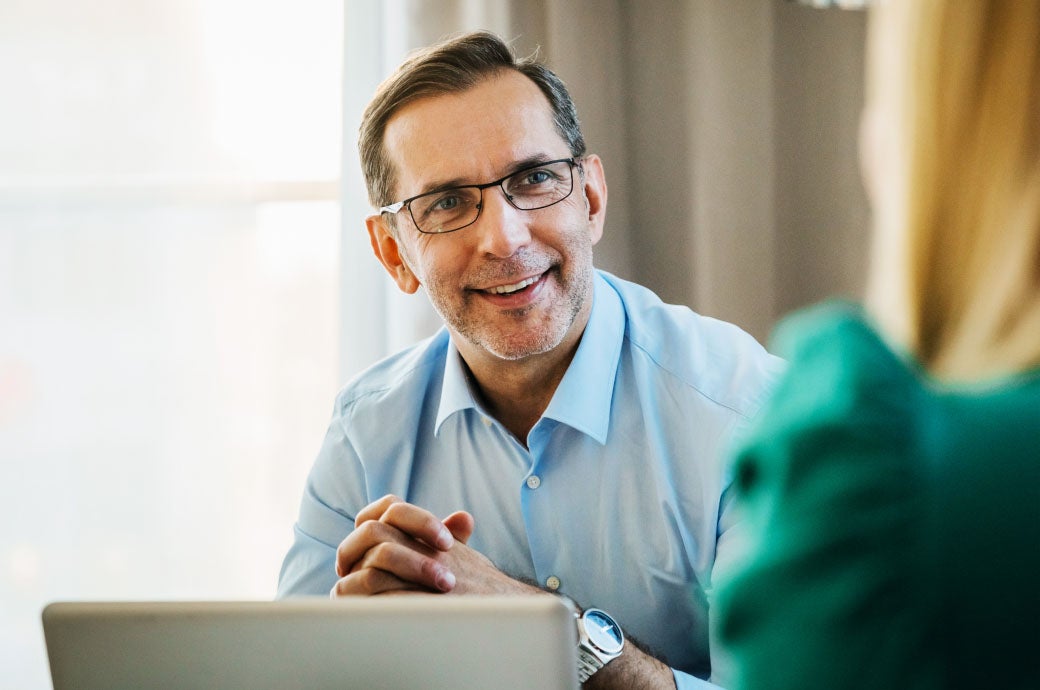 Close-up of man with glasses consulting with a woman who is holding a laptop computer