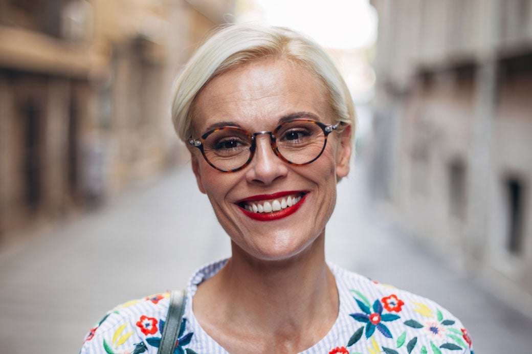 Smiling woman wearing glasses and brightly colored shirt.
