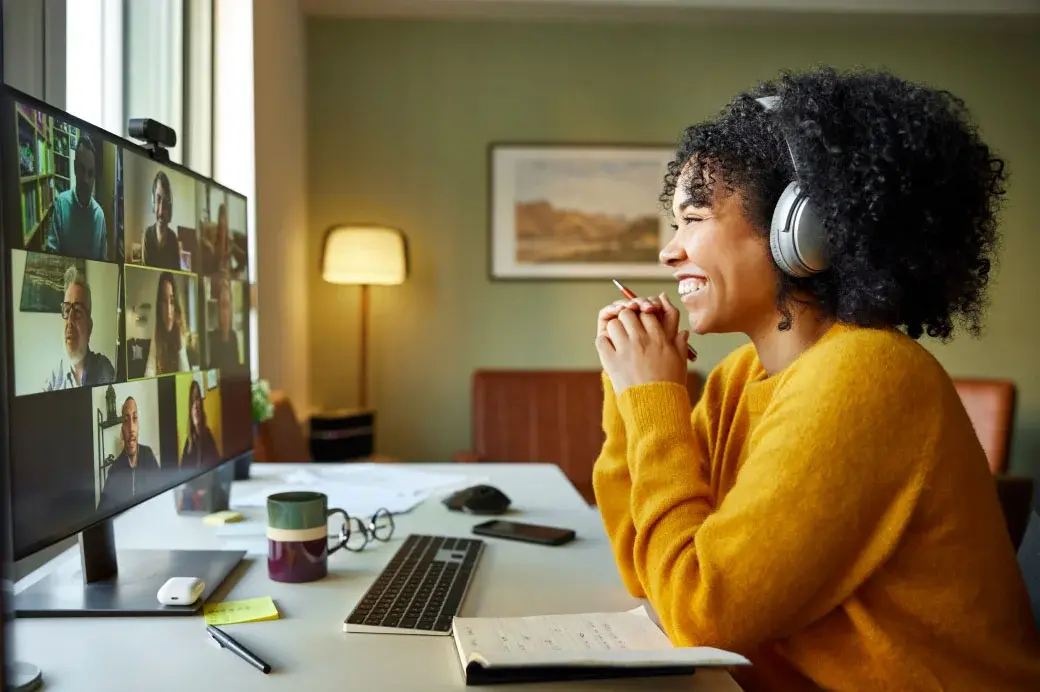 Smiling woman with headphones at a desk and on a zoom call