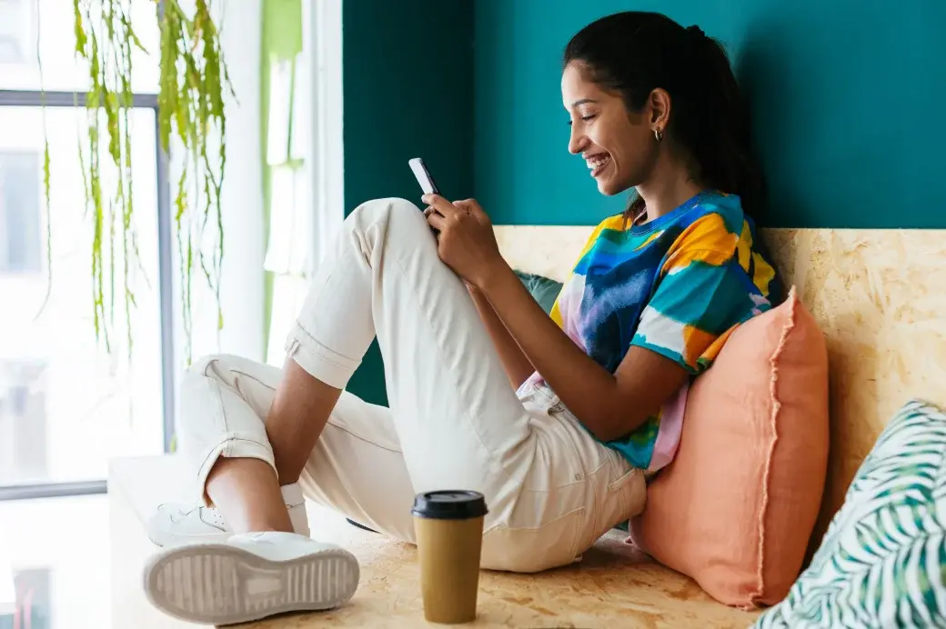 Smiling young woman sitting on a couch looking at her smartphone.
