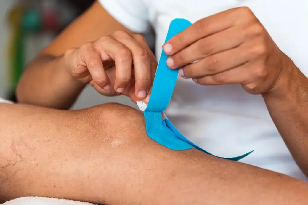 Hands of a healthcare worker applying a bandage on a patient’s knee.