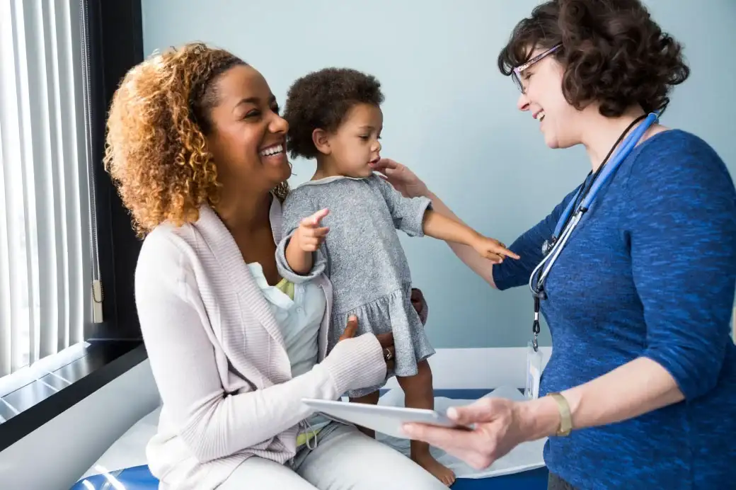 Woman holding a pediatric patient and smiling at a physician who is examining the child